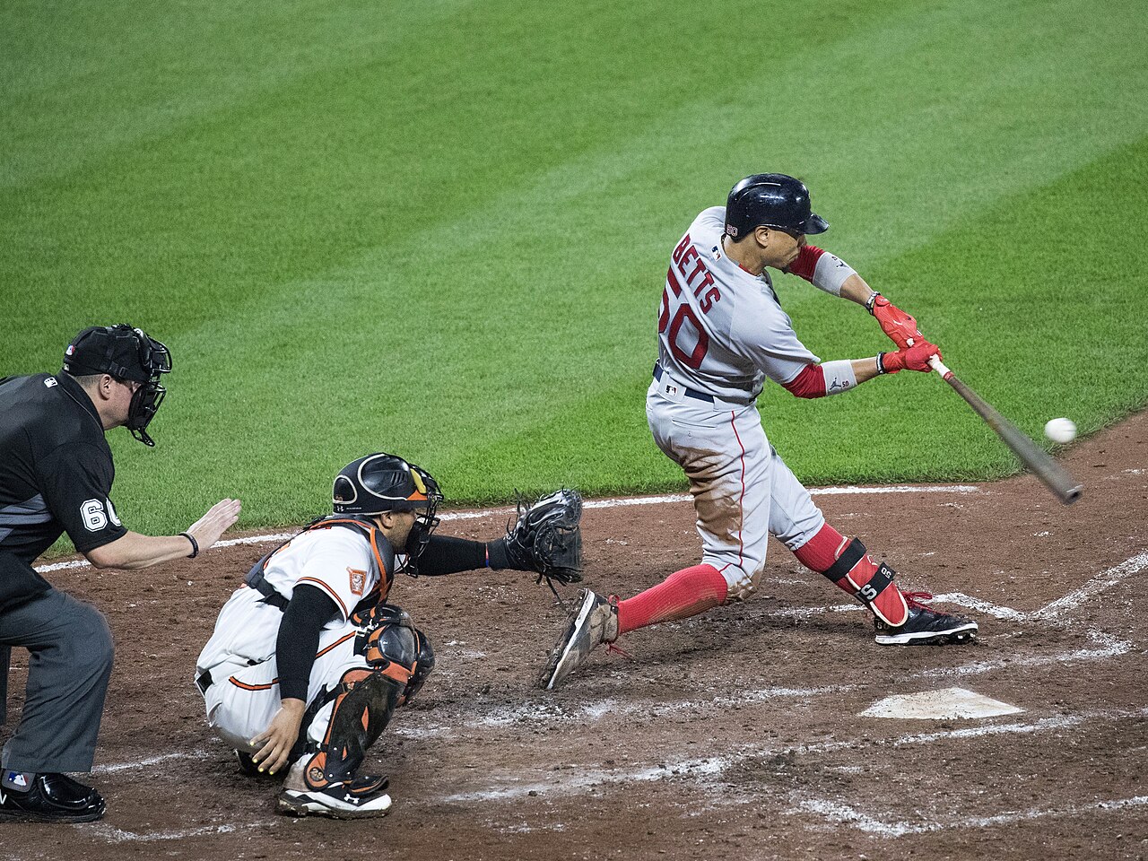 Mookie Betts makes contact with a pitched baseball as the catcher and home-plate umpire follow the play.